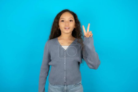 Photo for Beautiful kid girl wearing casual jacket over blue background showing and pointing up with fingers number two while smiling confident and happy. - Royalty Free Image