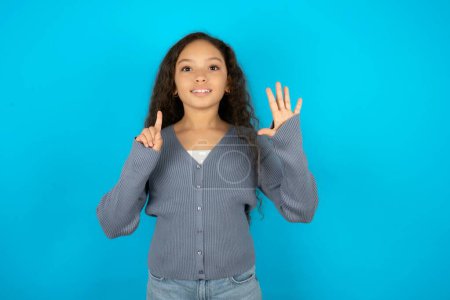 Foto de Hermosa niña con chaqueta casual sobre fondo azul mostrando y apuntando hacia arriba con los dedos número seis mientras sonríe confiado y feliz. - Imagen libre de derechos