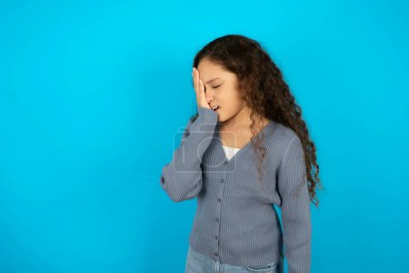 Téléchargez les photos : Belle jeune fille portant une veste décontractée sur fond bleu bâillement fatigué couvrant la moitié du visage, des yeux et de la bouche avec la main. Le visage souffre dans la douleur. - en image libre de droit