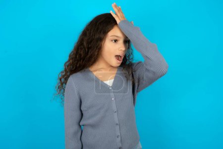 Photo for Beautiful kid girl wearing casual jacket over blue background surprised with hand on head for mistake, remember error. Forgot, bad memory concept. - Royalty Free Image