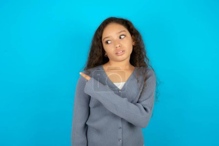 Photo for Beautiful kid girl wearing casual jacket over blue background Pointing aside worried and nervous with forefinger, concern and surprise concept. - Royalty Free Image