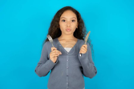 Photo for Hungry Beautiful kid girl wearing casual jacket over blue background holding in hand fork knife want tasty yummy pizza pie - Royalty Free Image