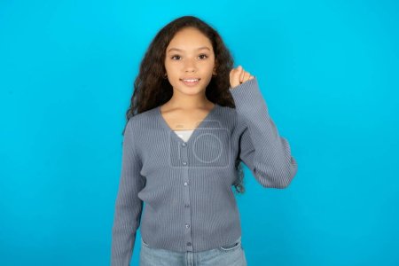 Foto de Hermosa niña con chaqueta casual sobre fondo azul apuntando hacia arriba con los dedos número diez en chino lenguaje de signos Shi - Imagen libre de derechos
