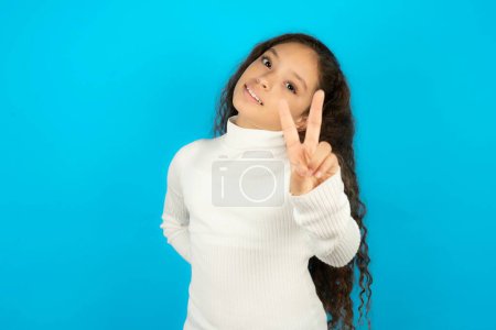 Photo for Beautiful kid girl wearing white turtleneck over blue background directs fingers at camera selects someone. I recommend you. Best choice - Royalty Free Image