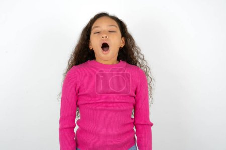 Foto de Hermosa niña con cuello alto rosa sobre fondo blanco bosteza con la boca abierta se levanta. Rutina diaria - Imagen libre de derechos