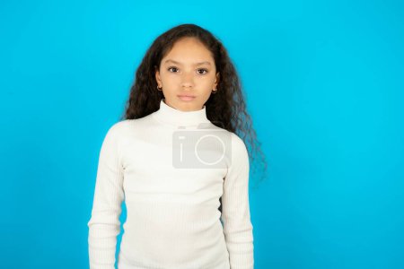 Photo for Displeased Beautiful kid girl wearing white turtleneck over blue background frowns face feels unhappy has some problems. Negative emotions and feelings concept - Royalty Free Image