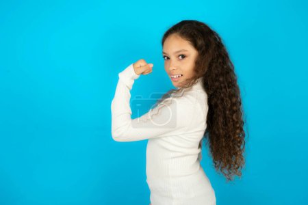 Photo for Profile side view portrait Beautiful kid girl wearing white turtleneck over blue background celebrates victory - Royalty Free Image