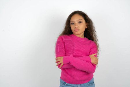 Foto de Hermosa niña confiada con cuello alto rosa sobre fondo blanco con los brazos cruzados mirando a la cámara - Imagen libre de derechos