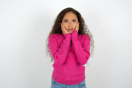 Photo for Upset Beautiful kid girl wearing pink turtleneck over white background touching face with two hands - Royalty Free Image