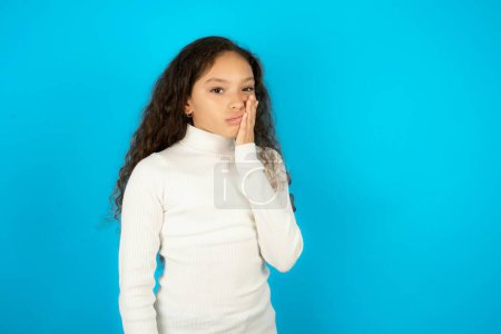 Photo for Beautiful kid girl wearing white turtleneck over blue background with toothache - Royalty Free Image