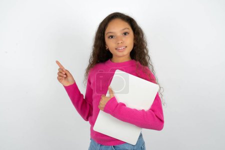 Foto de Hermosa niña con cuello alto rosa sobre fondo blanco celebración de la computadora portátil que muestra copia de espacio vacío anuncio - Imagen libre de derechos