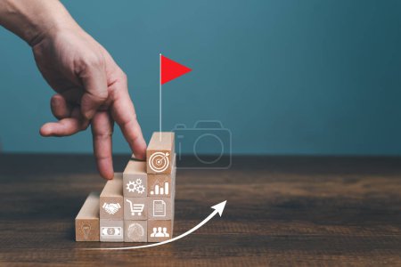 Step by step to grow your business, business success or career path success concept. Man use finger walking up to the top target with red flag on wooden blocks arranged in a shape of staircase.