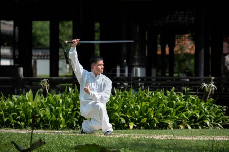 Téléchargez les photos : Jeune homme pratiquant l'épée traditionnelle de Tai Chi, Tai Ji dans le parc pour sain, traditionnel chinois concept d'arts martiaux sur fond naturel . - en image libre de droit
