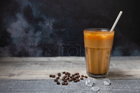 Ice coffee in a tall glass. Cold summer drink on a dark wooden background with copy space. A refreshing drink in summer. 