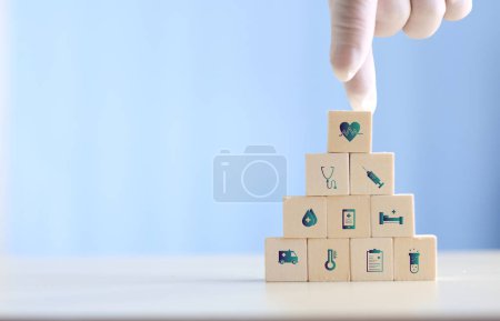 Foto de Doctor arranging and stacking wooden block cubes with printed screen health care and medical icons for the concept of health and wellness. Hand-arranging a wood block with a medical icons. - Imagen libre de derechos