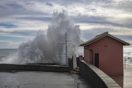 Foto de Una gran ola cerca de una pequeña casa en un día nublado con mar agitado en Génova, Italia - Imagen libre de derechos