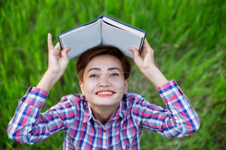 Téléchargez les photos : Femme heureuse allongée sur l'herbe verte lisant un livre dans le parc (en plein air) SSTKHome - en image libre de droit