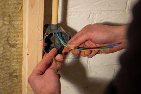 Bau und Installation von elektrischen Leitungen mit der Braunphase, dem blauen Neutral- und dem gelben Erdkabel in einem Haus unter Verwendung von Hohlraumwandgehäusen