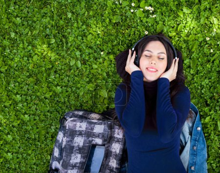 Téléchargez les photos : Portrait de jeune femme mignonne écoutant de la musique avec écouteurs en plein air. Copier l'espace sur l'herbe verte. - en image libre de droit