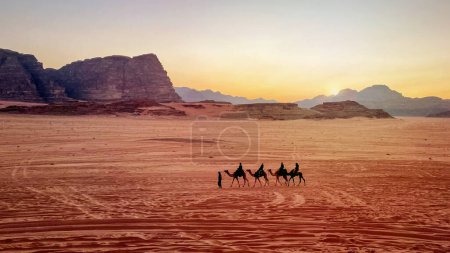 Foto de Jordan, Wadi Rum. Caravana de camellos con manadas en el desierto, montañas rocosas al atardecer. - Imagen libre de derechos