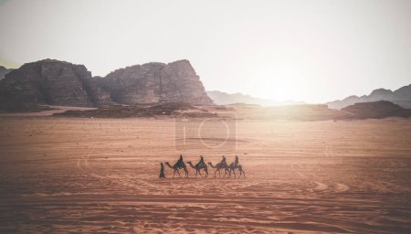 Foto de Jordan, Wadi Rum. Caravana de camellos con manadas en el desierto, montañas rocosas al atardecer. - Imagen libre de derechos