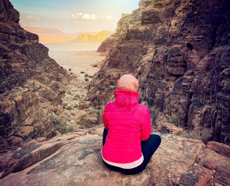 Photo for Woman tourist sits on a stone ledge against the backdrop of the mountains in the Wadi Rum desert at sunset. - Royalty Free Image