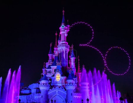Foto de París, Francia - 02 de junio de 2023: Castillo iluminado para la exposición del 30 aniversario en el parque Disneyland Paris. Los drones dibujan los treinta y la silueta de Mickey Mouse en el cielo. - Imagen libre de derechos