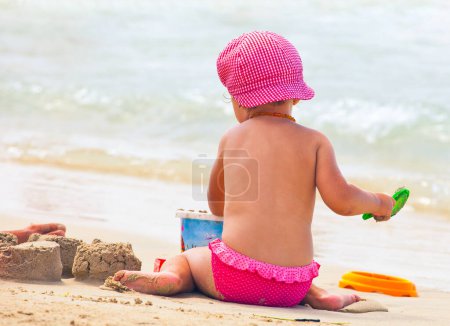 Foto de Pequeña niña juega en la costa en la playa con un sombrero. - Imagen libre de derechos
