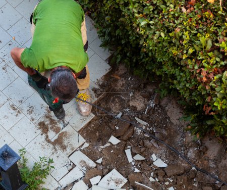 Téléchargez les photos : Travailleur enlève carreaux de jardin avec marteau-piqueur. - en image libre de droit