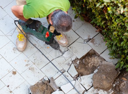 Photo for Worker removes garden tiles with jackhammer, top view. - Royalty Free Image
