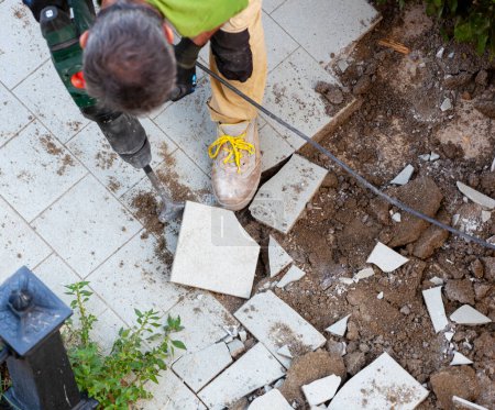 Téléchargez les photos : Travailleur enlève carreaux de jardin avec marteau-piqueur, vue de dessus. - en image libre de droit