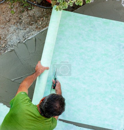 Téléchargez les photos : Tiler coupe tapis insonorisant avant de poser des tuiles. - en image libre de droit