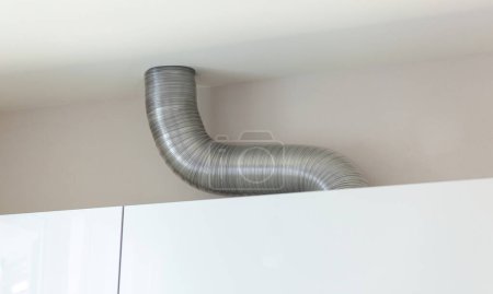 Téléchargez les photos : Tuyau de ventilation en aluminium ondulé extensible dans la cuisine reliant une hotte et un conduit d'air de ventilation. - en image libre de droit