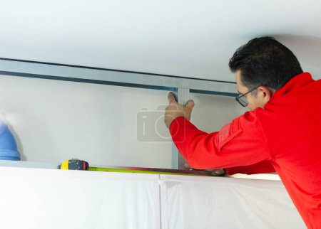 Plasterboard worker installs a plasterboard wall on the kitchen cabinets to cover the extractor pipe of the hood.
