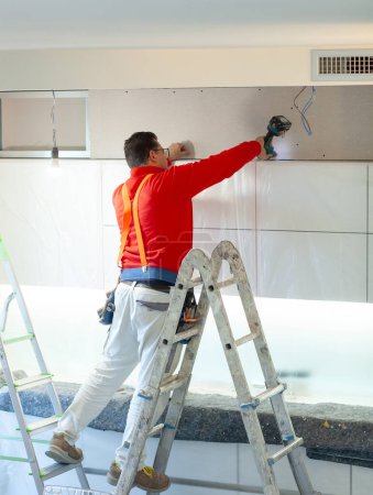 Foto de Trabajador de placas de yeso instala una pared de placas de yeso en los gabinetes de cocina para cubrir el tubo extractor de la campana. - Imagen libre de derechos