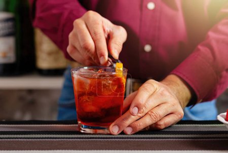 Primer plano de las manos de un camarero añadiendo una guarnición de cítricos a una copa de cóctel refrigerada