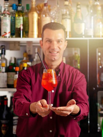 Lächelnder männlicher Barkeeper, der einen frisch zubereiteten Cocktail in einer modernen Bar anbietet