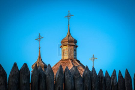 Zaporizhzhya Sich - chapel with three crosses on its facade stands behind a wooden fence under a blue sky. The citys tints and shades reflect in the windows, adding to the serenity of the scene