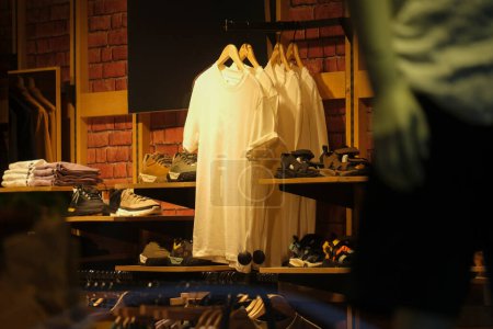 Intérieur d'un magasin de vêtements avec des t-shirts blancs et des baskets exposées, éclairées par un éclairage chaleureux, créant un environnement commercial confortable et accueillant