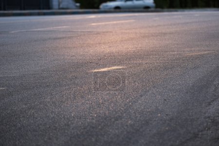 Gros plan d'une route asphaltée vide avec un coucher de soleil chaud, soulignant la texture de la chaussée et un fond flou