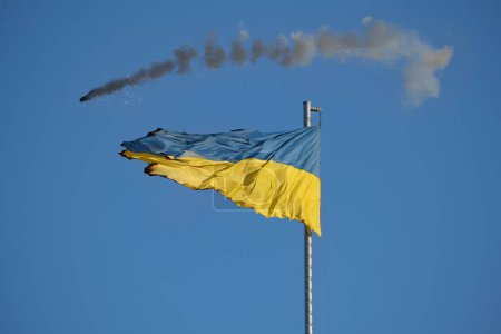 Drapeau ukrainien brisé flottant contre un ciel bleu clair, avec des signes visibles d'usure et de dommages, symbolisant la résilience et l'endurance.