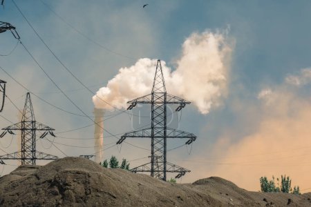 Eine Nahaufnahme von Stromleitungen und Rauchentwicklung aus einem industriellen Schornstein. Das Bild betont die Umweltauswirkungen der industriellen Umweltverschmutzung und der Infrastruktur zur Energieerzeugung.