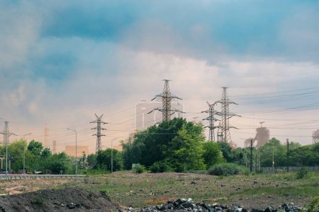 An industrial landscape with power lines and smoke emissions. Environmental impact of industrial activities, emphasizing pollution and infrastructure in a mixed natural and industrial setting.