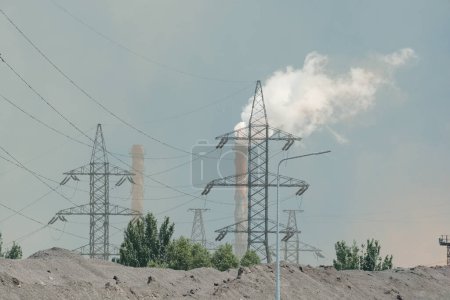 Eine Industrieszene mit Stromleitungen und Rauchschwaden aus Schornsteinen an einem heißen Tag. Das Bild unterstreicht die Auswirkungen industrieller Aktivitäten auf die globale Erwärmung und den Klimawandel