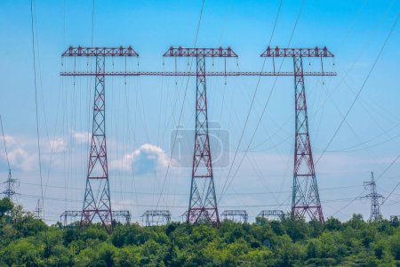 High voltage power lines tower over a lush green landscape against a clear blue sky. This image highlights the intersection of energy infrastructure and natural environments