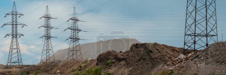 A wide panoramic view of an industrial landscape featuring power lines. Industrial impact on the environment. Mountains of rock and slag from iron ore.