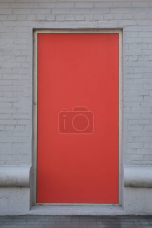 Nahaufnahme einer leuchtend roten Tür vor einer weißen Backsteinwand, die eine perfekte, leere Leinwand für Werbung, Schilder oder kreative Designprojekte bietet. Für Werbeflächen und städtebauliche Artikel