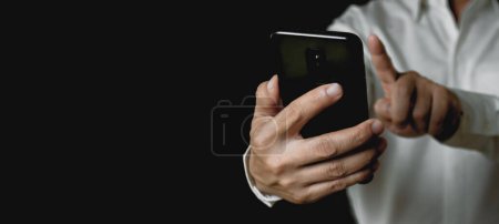 Téléchargez les photos : Homme d'affaires tenant la main et utilisant un smartphone Sur fond noir, concept de technologie de communication travail sur les réseaux sociaux en ligne - en image libre de droit