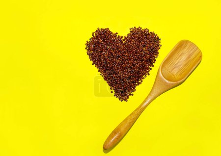 Foto de Semilla de quinua roja sin cocer en forma de corazón con cuchara de madera sobre fondo amarillo. - Imagen libre de derechos