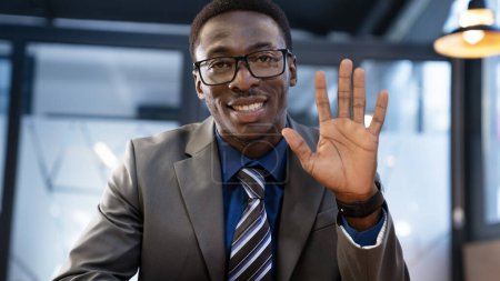 Téléchargez les photos : Jeune homme d'affaires agitant la main sur appel vidéo au bureau - en image libre de droit